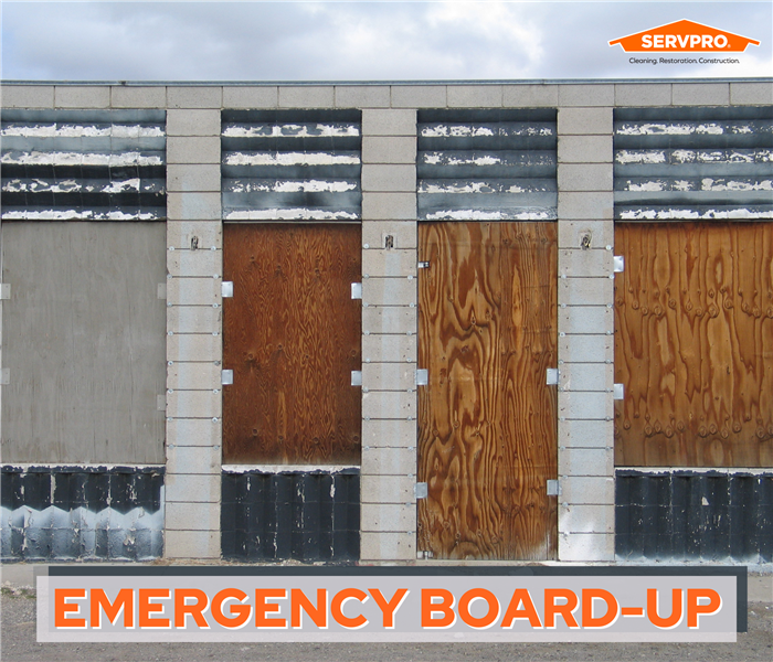 boarded up windows, industrial building, plywood doors, text that says "emergency board up" in corner orange servpro logo